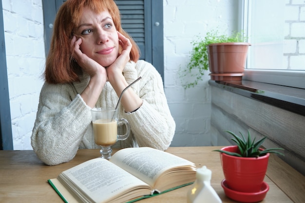 Adult woman relaxing at home with mug of hot beverage and book in kitchen