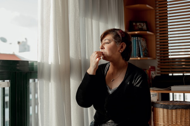 Adult woman with short hair spending time sitting and relaxing in her studio while eating some peanuts. Spending time to relax in quarantine.