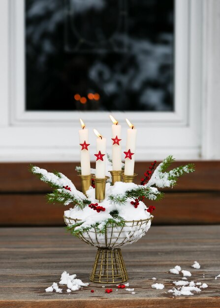 Advent wreath with four white burning candles and red wooden stars in a metal basket full of snow