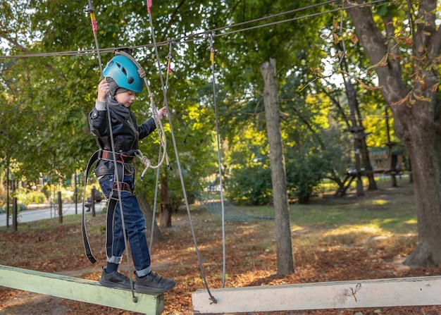 Adventure climbing high wire park. Brave young child in safety harness climb high on tree tops. Active lifestyle in scout camp. Little boy playing and having fun doing activities outdoors.