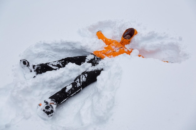 Adventure man in a colorful outfit is making snow angel