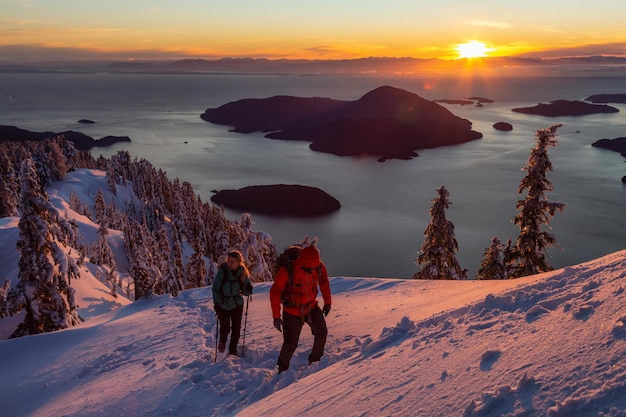 Adventure seeking man and woman are hiking to the top of a mountain during winter sunset