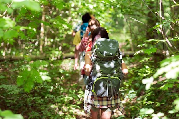 adventure, travel, tourism, hike and people concept - close up of friends walking with backpacks in woods from back