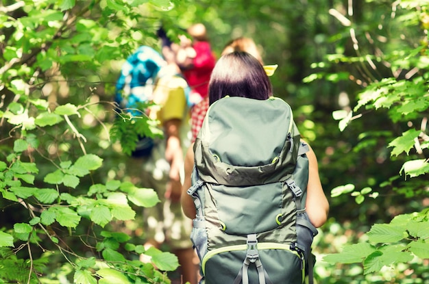 adventure, travel, tourism, hike and people concept - close up of friends walking with backpacks in woods from back