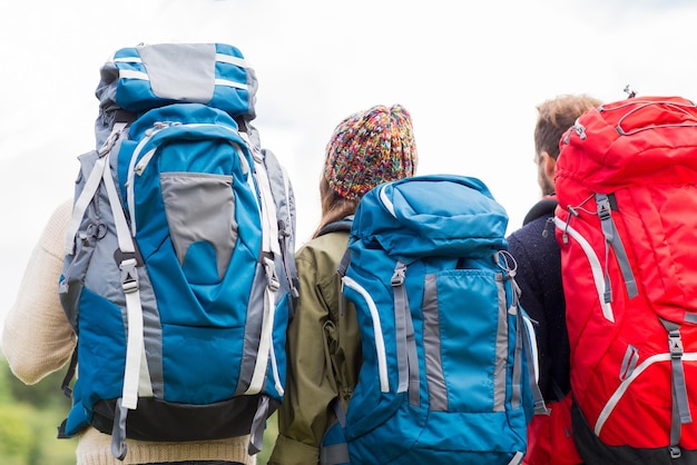 adventure, travel, tourism, hike and people concept - group of friends walking with backpacks from back