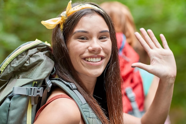 adventure, travel, tourism, hike and people concept - group of smiling friends walking with backpacks in woods