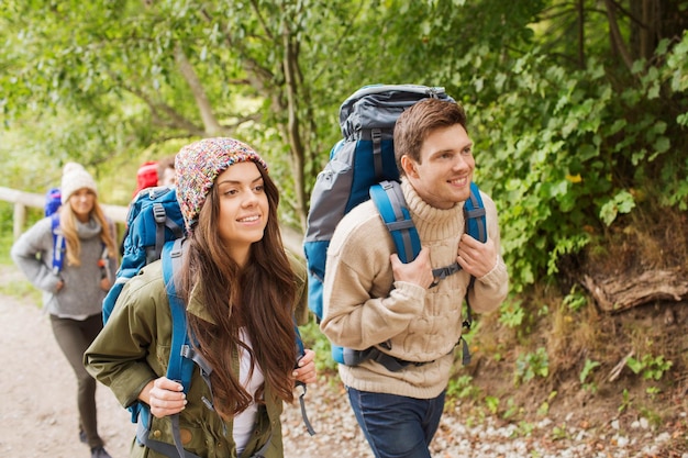 adventure, travel, tourism, hike and people concept - group of smiling friends walking with backpacks