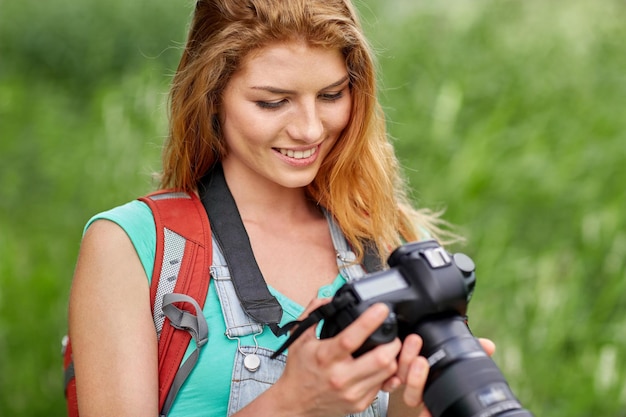 adventure, travel, tourism, hike and people concept - happy young woman with backpack and camera photographing outdoors