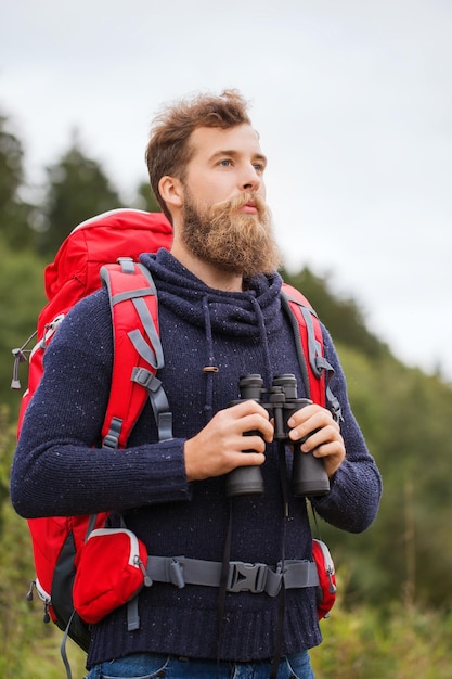 adventure, travel, tourism, hike and people concept - man with red backpack and binocular outdoors