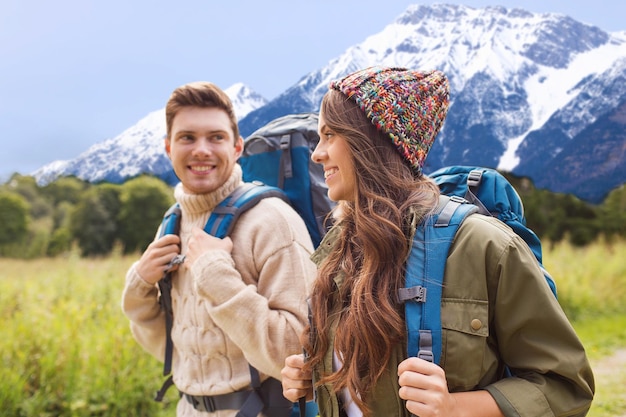 adventure, travel, tourism, hike and people concept - smiling couple walking with backpacks over mountains background