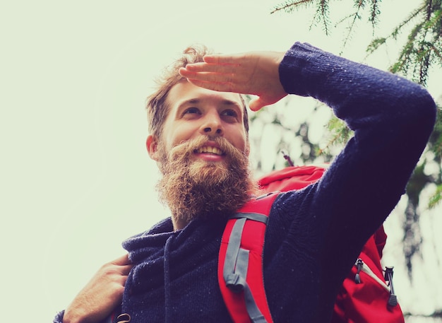 adventure, travel, tourism, hike and people concept - smiling man with beard and red backpack hiking