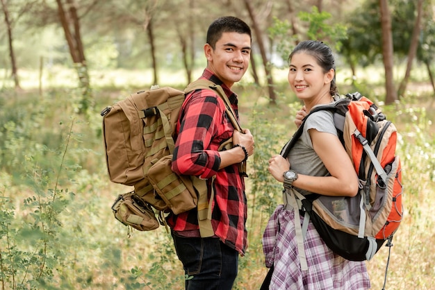 Adventure and Trekking Concept, Asian backpacker men and women carrying a big bag, walking into the forest and looking back.