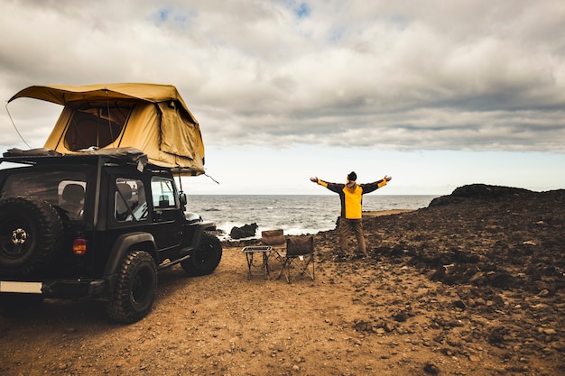 Adventurer man in journey travel with off road car and roof tent to enjoy freedom and explorer concept discover the world living near the power of the nature ocean coast home view