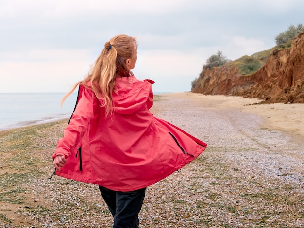 Photo the adventures of alone girl in a pink raincoat on the seashore