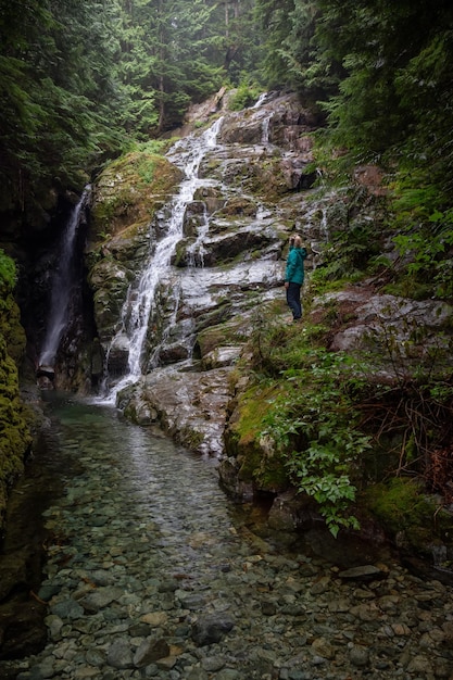 Adventurous female hiker is enjoying a view of a waterfall during a foggy day