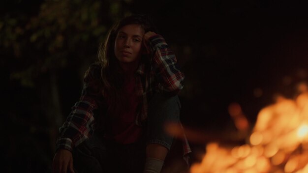 Adventurous girl enjoy campfire burning on dark night outdoors Close up young millennial woman watch look bonfire on relaxing evening Tired tourist rest on nature journey Leisure vacation concept