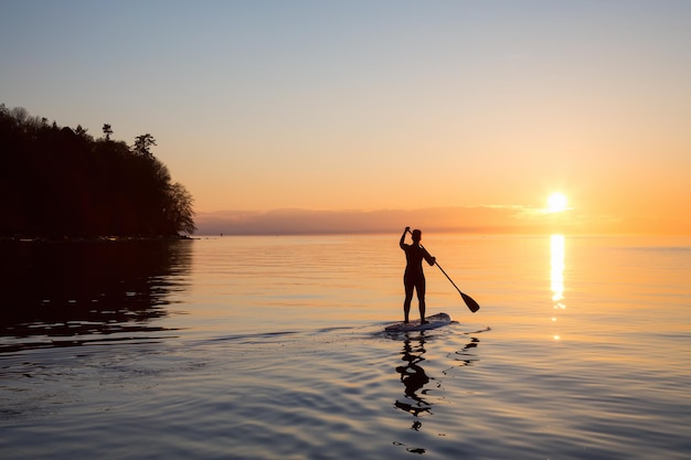 Adventurous girl on a paddle board is paddeling during a bright and vibrant sunset