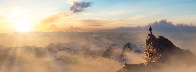 Adventurous Man Hiker standing on top of icy peak with rocky mountains in background