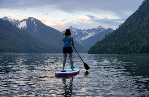 Adventurous woman paddle boarding in a lake around canadian mountain landscape