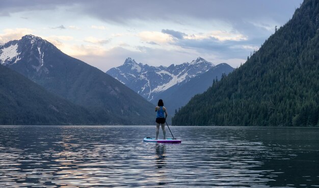 Adventurous woman paddle boarding in a lake around canadian mountain landscape