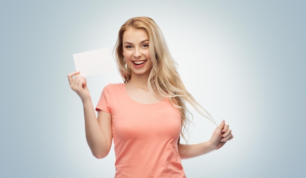 advertisement, invitation, message and people concept - smiling young woman or teenage girl with blank white paper card over gray background