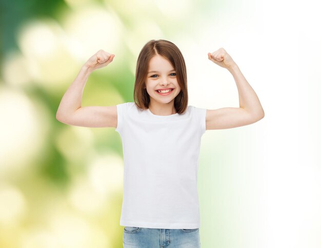 advertising, childhood, gesture, ecology and people - smiling little girl in white blank t-shirt with raised arms over green background