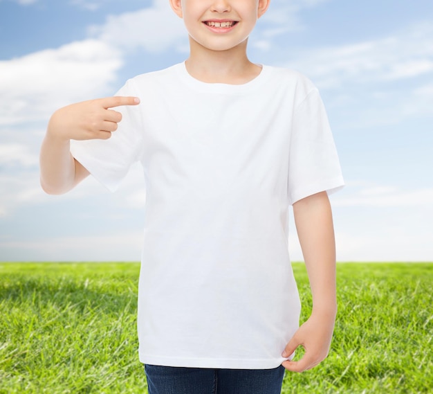 advertising, people, childhood and t-shirt design concept - smiling little boy in white blank t-shirt pointing finger at himself over blue burst rays background