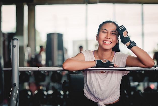 Aegean woman resting at the exercise table After sports training with dumbbells. Concept: Sporty girl sitting in the gym.