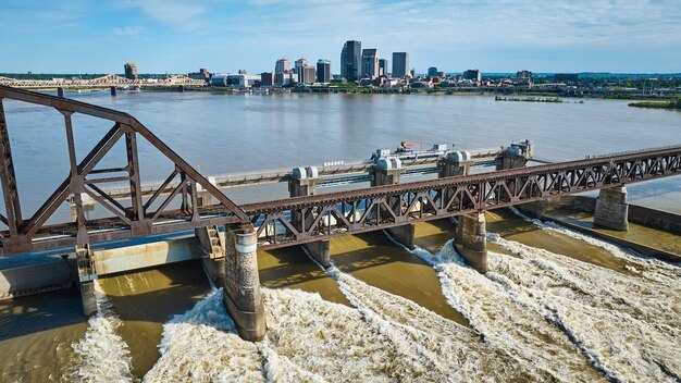 Photo aerial brown truss arch bridge over dam in ohio river white water rapids louisville city skyline