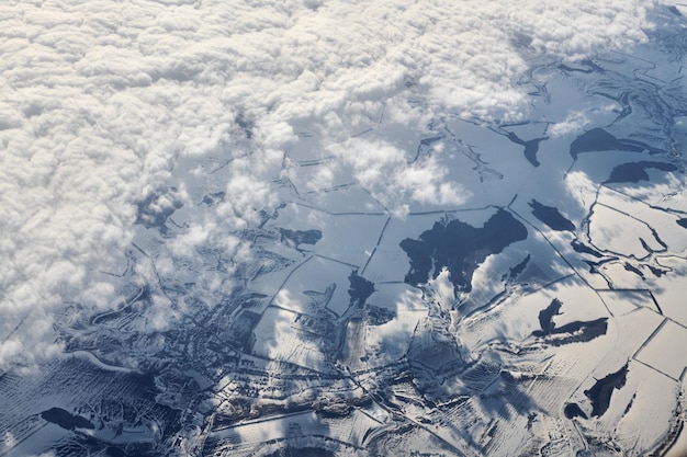 Aerial cloudscape view over clouds top to snow covered rivers roads cities and fields winter air