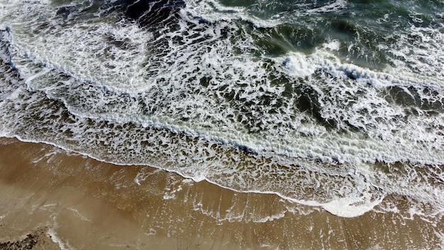 Aerial drone view flight over sea waves that roll onto sandy shore