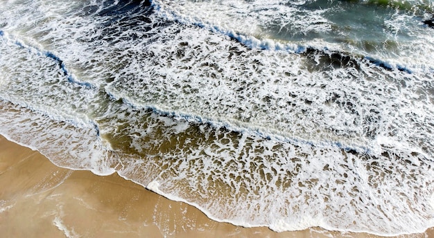 Aerial drone view flight over sea waves that roll onto sandy shore