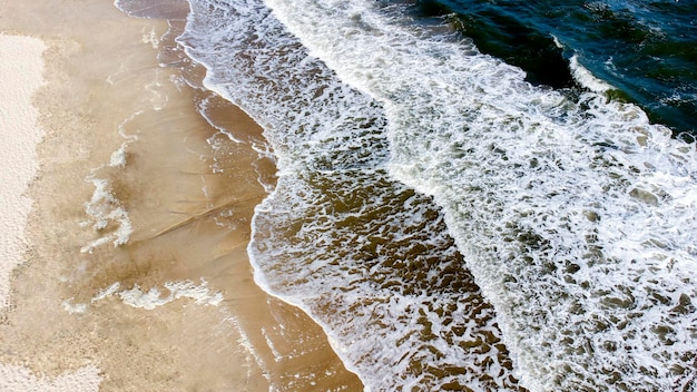 Aerial drone view flight over sea waves that roll onto sandy shore