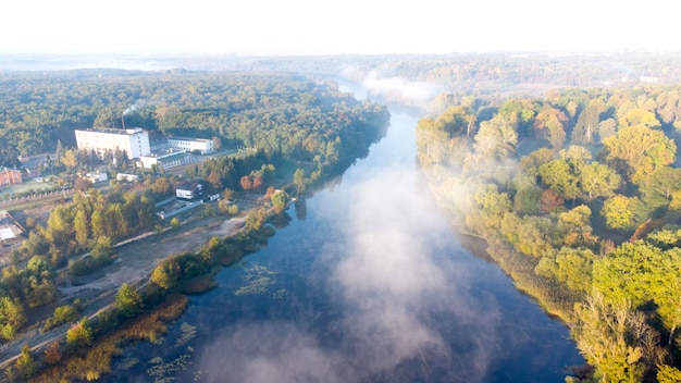 Aerial drone view flying over the river with calm reflective water surface and white fog mist and fo