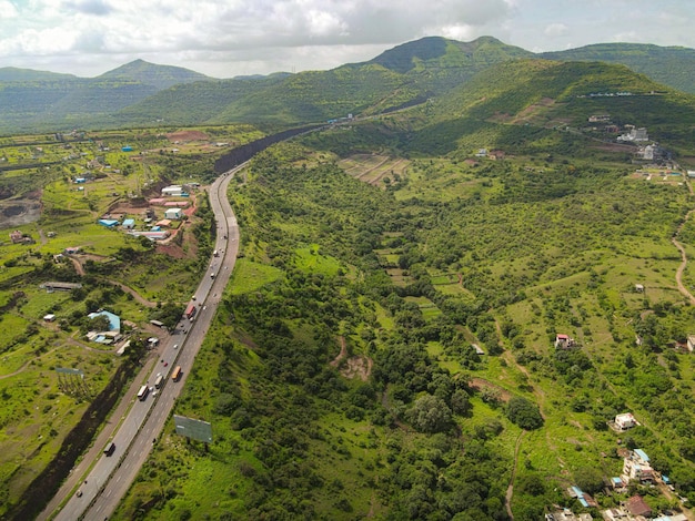 Aerial drone view of Pune Bangalore highway surrounded by green valley and mountains on cloudy day