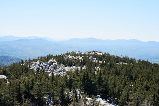 Aerial image of white massive rocks surrounded by conifer woods and high mountains in the distance o