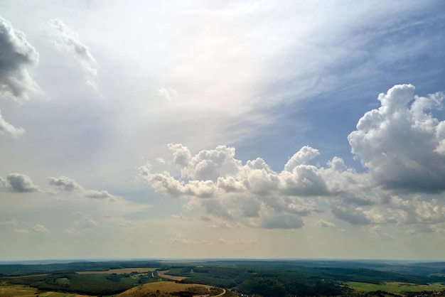 Aerial landscape view of clear blue sky over green cultivated agricultural fields with growing crops and distant woodland on bright summer day