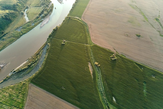 Aerial landscape view of village houses and distant green cultivated agricultural fields with growing crops on bright summer day