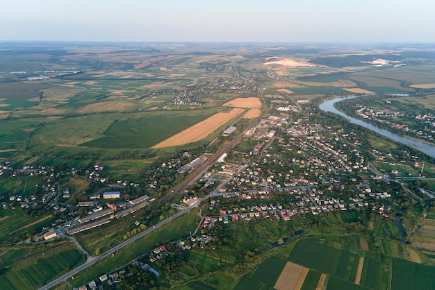 Aerial landscape view of village houses and distant green cultivated agricultural fields with growing crops on bright summer day