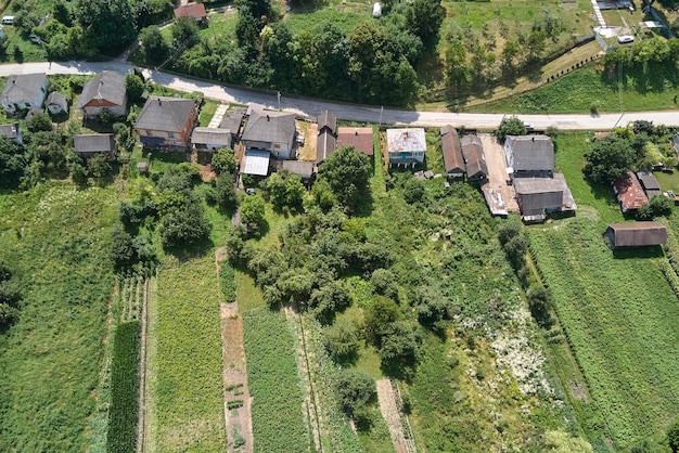 Aerial landscape view of village houses and distant green cultivated agricultural fields with growing crops on bright summer day