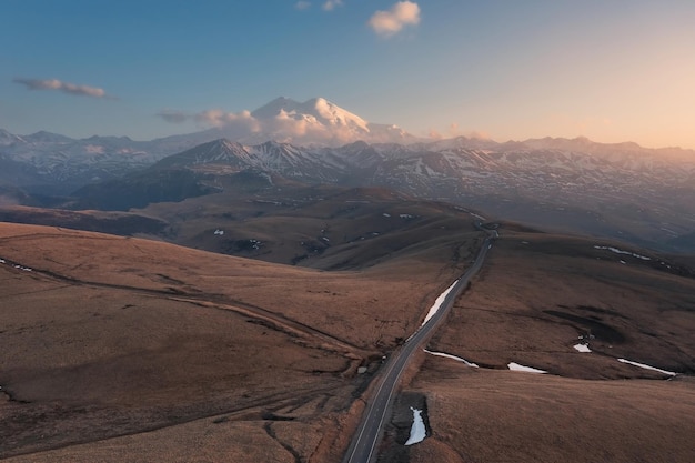 Aerial landscape with road going along hilltops to snowcovered high mountain MtElbrus Russia