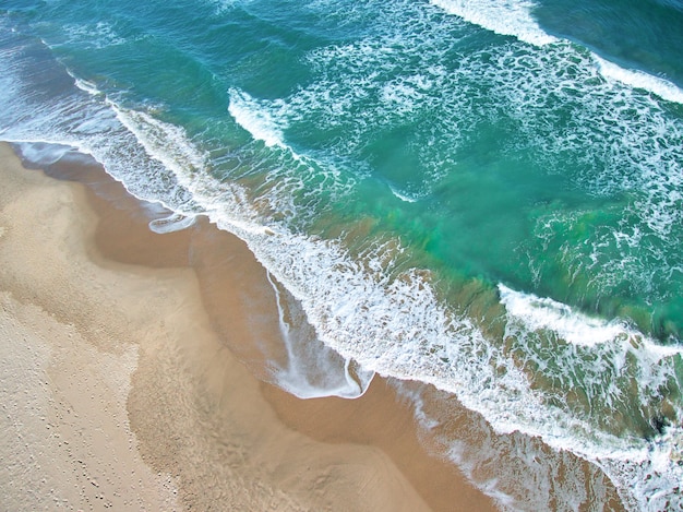 Aerial overhead shot of the foam of the sea waves with orange sand and green water