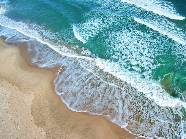 Aerial overhead shot of the foam of the sea waves with orange sand and green water