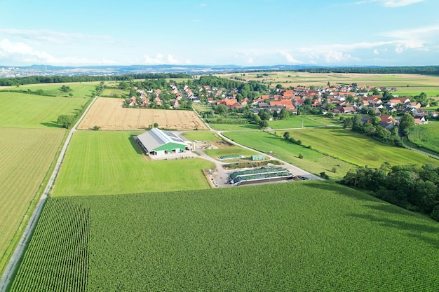 Aerial shot of a cow farmer business with a beautiful vilylage next to it surrounded by nature