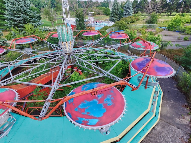 Aerial shot of a tilt a whirl at an abandoned theme park surrounded by trees and grasses