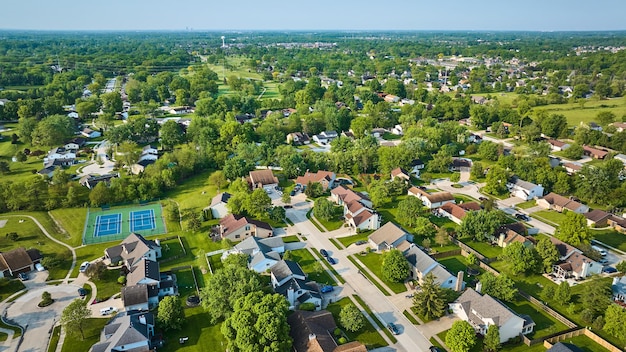 Aerial suburban neighborhood with trees and tennis court amenity distant water tower