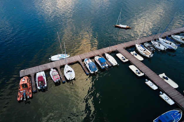 Aerial top view of boats and small jachts near wooden pier at the lake summer entertainment at water