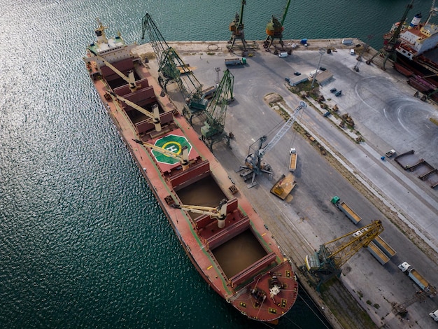 aerial top view of a bustling seaport where a massive cargo ship a bulk carrier is being loaded with wheat grains