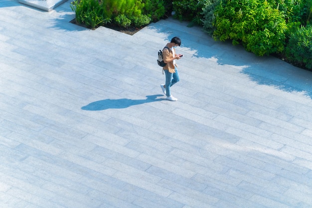 Aerial top view of man with face mask walks on across pedestrian street with black silhouette shadow on ground, concept of social new normal life prevention of covid pandemic and air pollution.