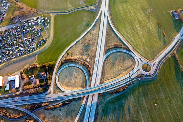 Aerial top view of modern highway road intersection, house roofs on spring green field. Drone photography.